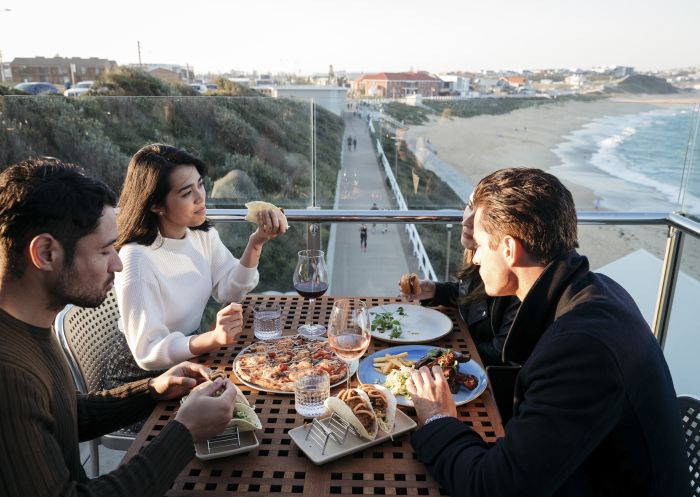 Friends enjoying food and drink with ocean views at Merewether Surfhouse in Newcastle.