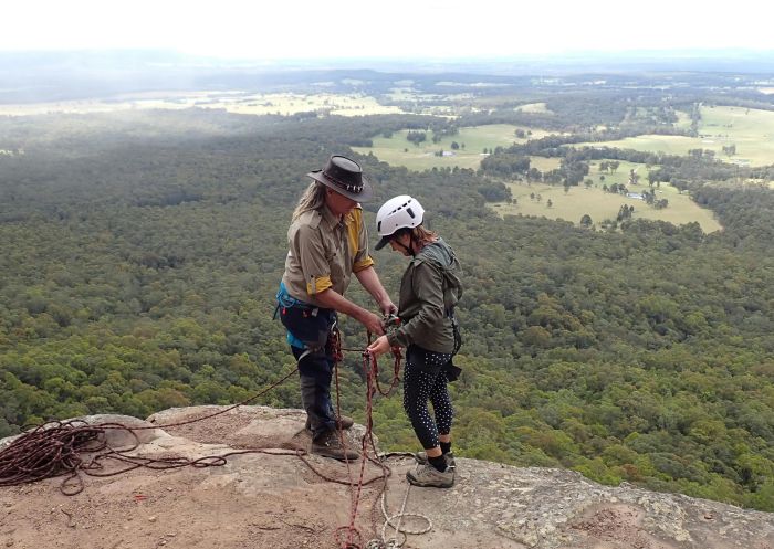 A guide and client are standing on top of a sixth meter abseiling cliff in Watagans National Park with Walking Rivers Pty Ltd