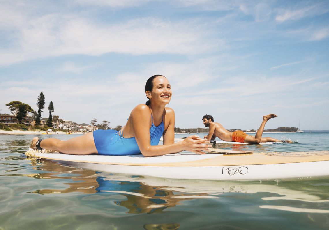 Couple enjoying a stand up paddleboarding experience in Shoal Bay, Port Stephens, North Coast