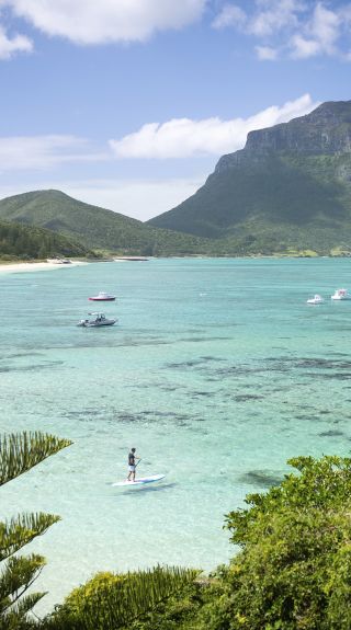 Man stand up paddleboarding off Lagoon Beach with views across to Mount Lidgbird