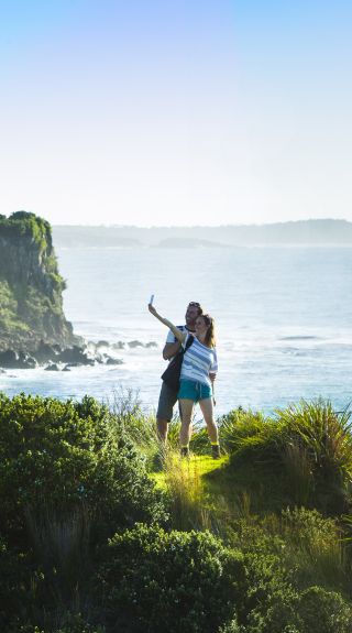 Couple taking photos on the scenic Minnamurra Headland overlooking Rangoon Island, Kiama Coast Walk, Kiama