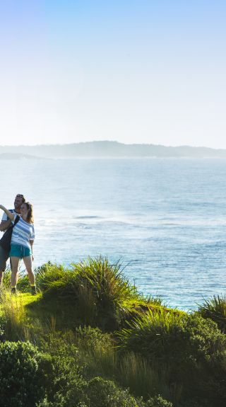 Couple taking photos on the scenic Minnamurra Headland overlooking Rangoon Island, Kiama Coast Walk, Kiama